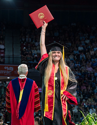 A student holds up their diploma at graduation