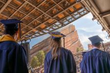 Three students in caps and gowns stand in line for their diploma at Red Rocks Amphitheatre.