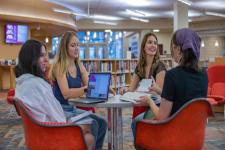 Four students sit in a circle with books and laptops. 