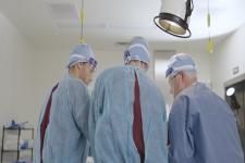 Three people in medical scrubs stand over an operating table. 