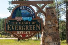 A rustic wooden sign reads "Welcome to the heart of Evergreen."