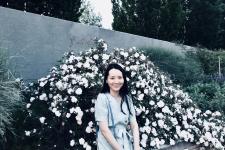 Mei Yin sits on a bench in front of a flowering bush.