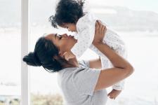 A young mother holds an infant up to her face and kisses them.