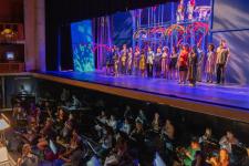 Wide photo of the stage and orchestra pit during the performance of an opera at the Newman Center.