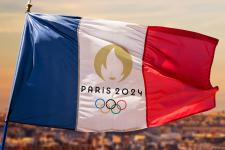 A French flag featuring the Olympic rings and the words Paris 24 flies on a flagpole over the city.