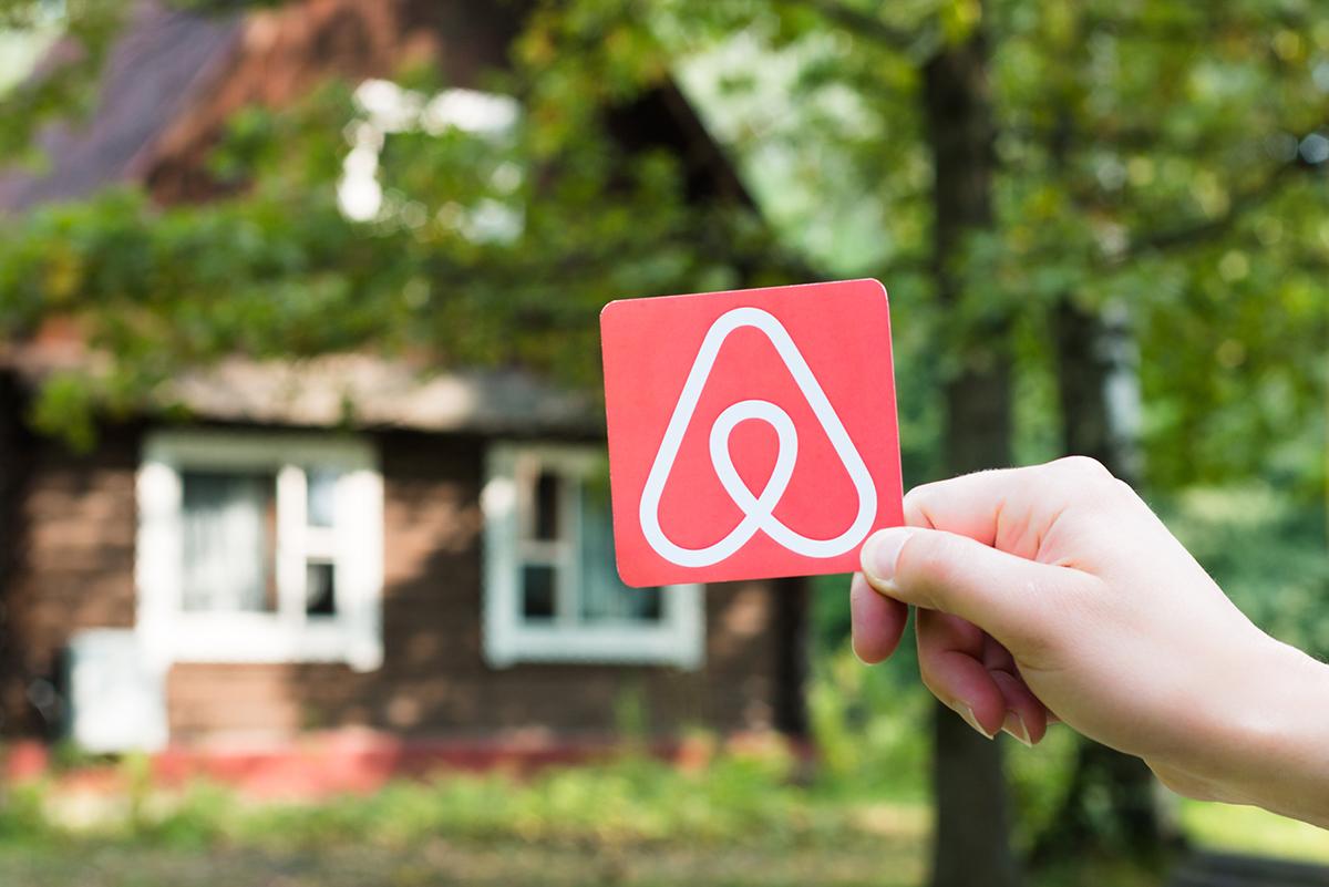 A hand holds a small piece of paper with the Airbnb logo on it.