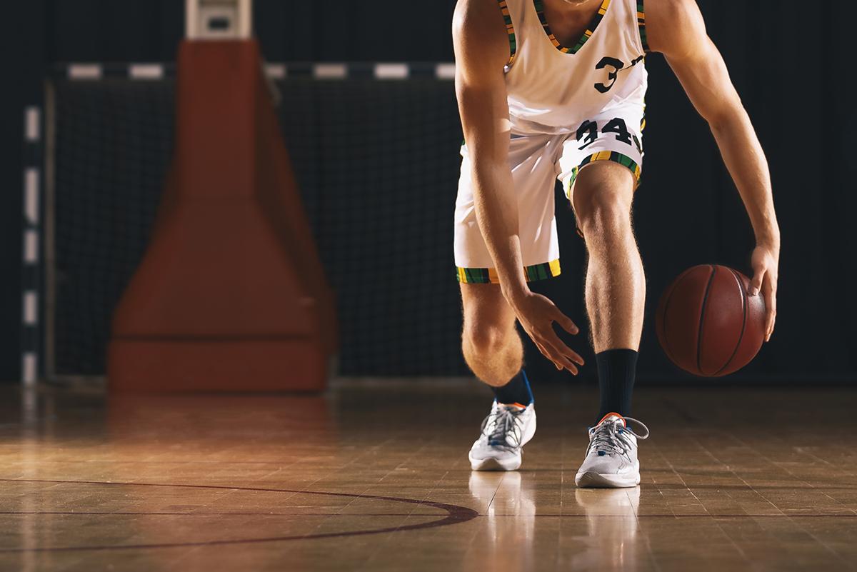 image of a basketball player from the neck down crouched and dribbling.