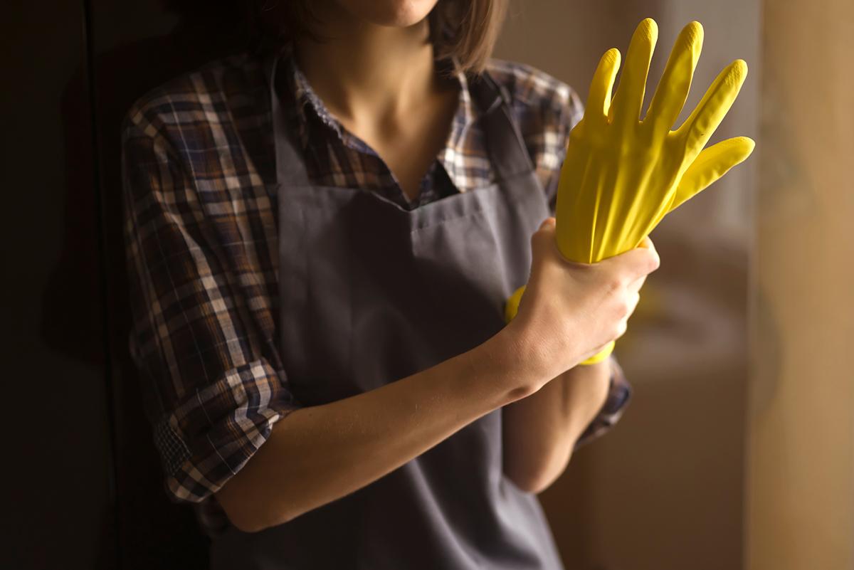 A woman holds her own hand that is inside a yellow rubber glove.