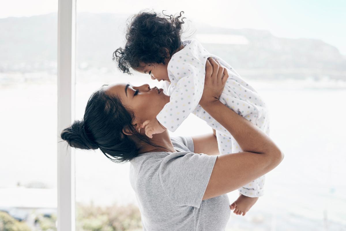 A young mother holds an infant up to her face and kisses them.