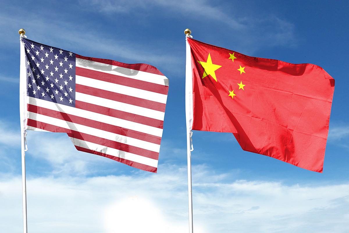 The American and Chinese flags fly on flagpoles side by side against a blue sky.