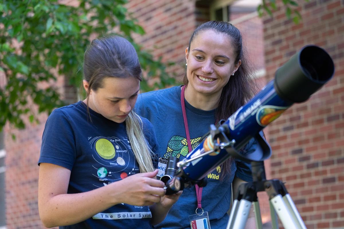 child with teacher and telescope outside