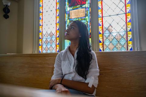 A student sits in front of stained glass in the Evans Chapel on the University of Denver campus. 