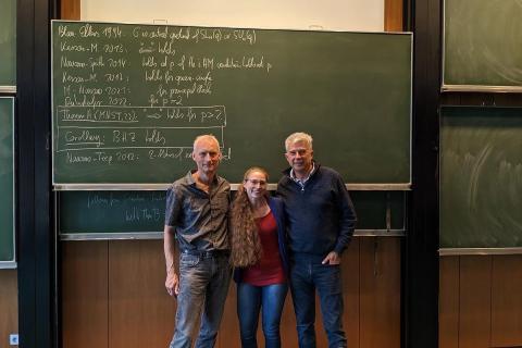 Three professors stand in front of a green chalkboard. 