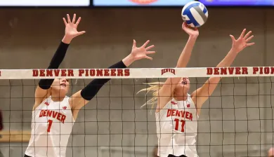 Dos jugadoras de voleibol femeninas bloquean en la red.