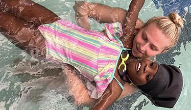 A DU swimmer helps a child in the pool learn how to float.
