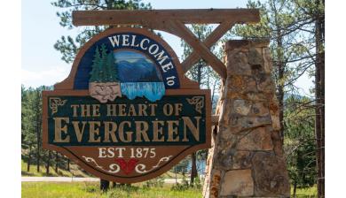 A rustic wooden sign reads "Welcome to the heart of Evergreen."