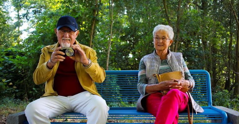 Two older adults sit on a park bench.