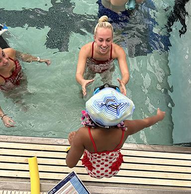 A DU swimmer helps a child jump into the pool.