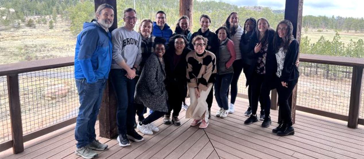 group of graduate students and professors posing on covered porch with forest in background