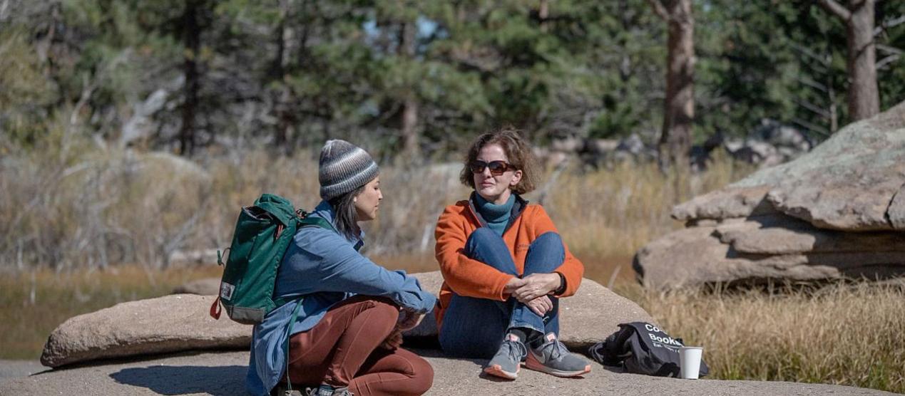 two people sitting and talking on a large rock