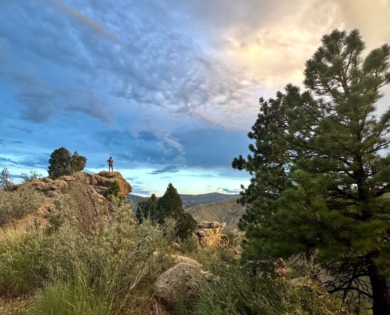 A landscape shot of a person standing on a large rock formation against a beautiful blue sky.